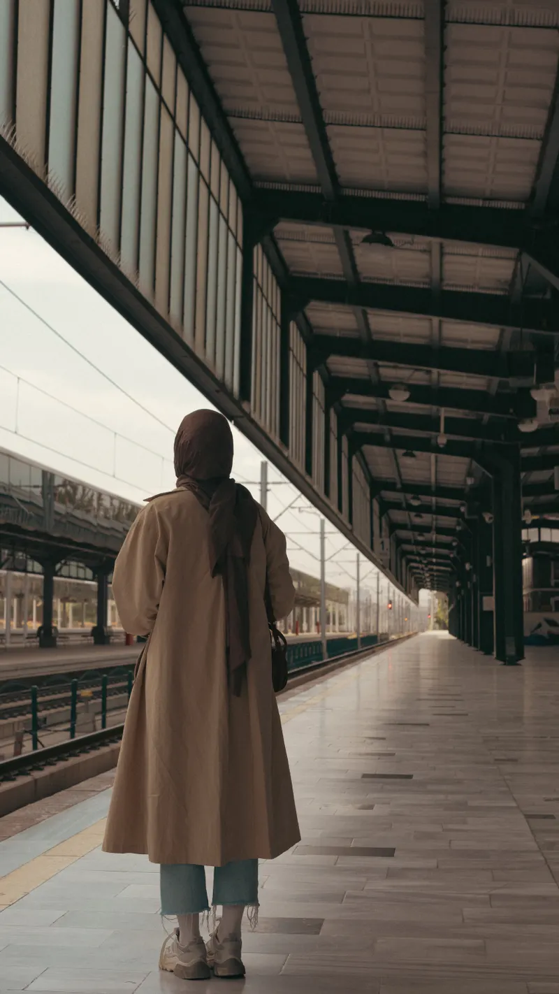 Bej uzun trençkot ve siyah şal giyen kadın, boş tren peronunda arkası dönük yürüyor