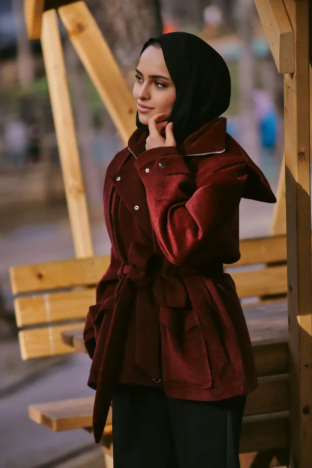 Bordo kuşaklı kaşe ceket ve siyah şal giyen kadın, ahşap bank yanında